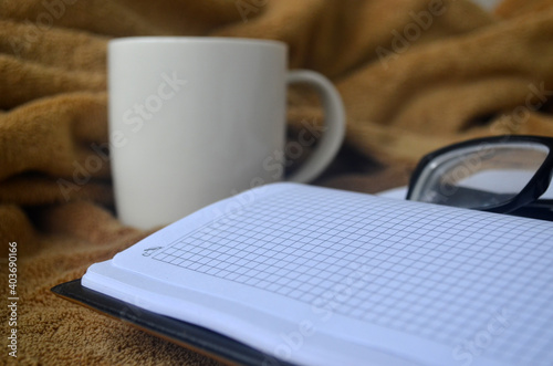 White mug with coffee and steam on a brown plaid, book, notebook