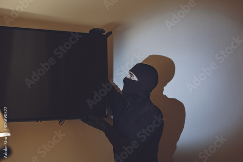 Full length of robber. Man with flashlight and bag in living room. Robber steals the TV/