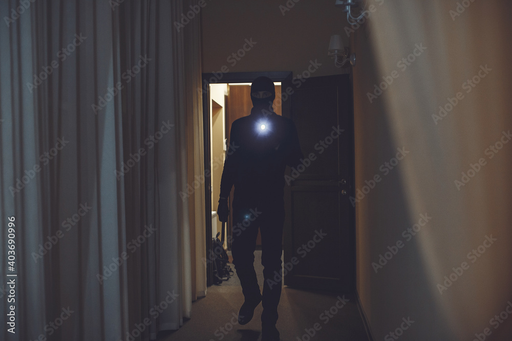 Full length of robber. Man with flashlight and bag in living room.