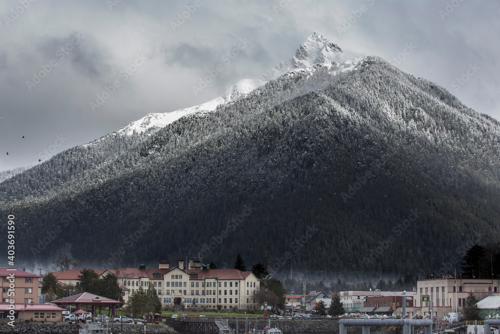 A towering snowcapped mountain sits in front of a small waterfront town in Alaska