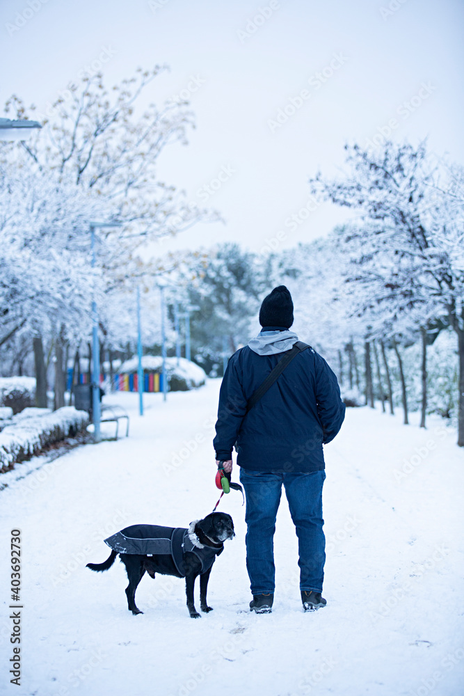 Hombre paseando con su perro en parque nevado.