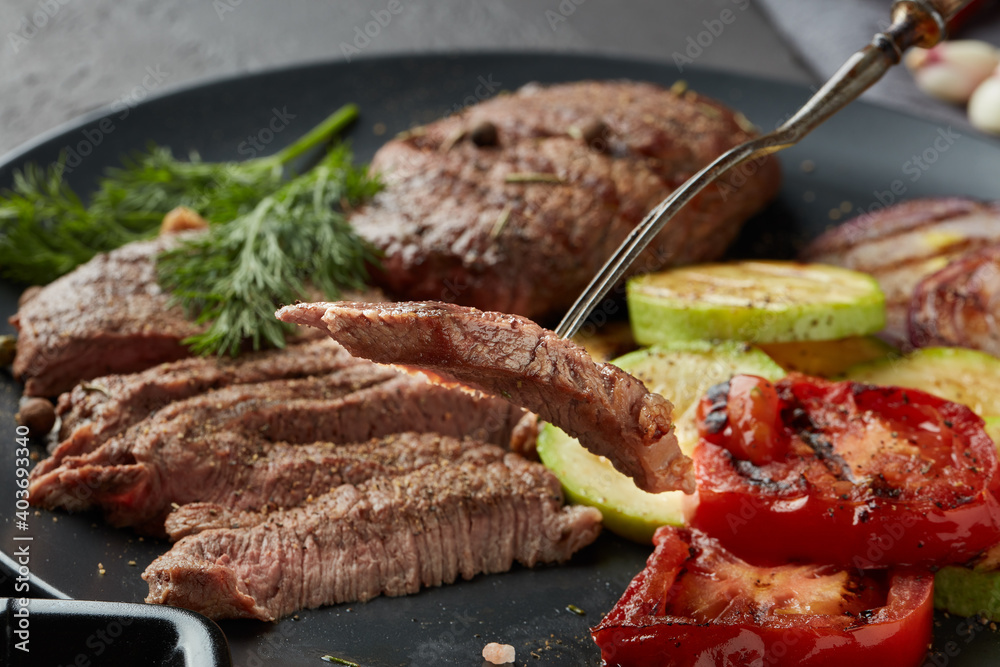 Grilled beef steak with spices and vegetables. Selective focus on slice of meat on fork