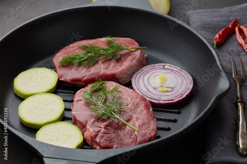 Beef steaks and cutting vegetables on grill pan on black slate background. Steak menu