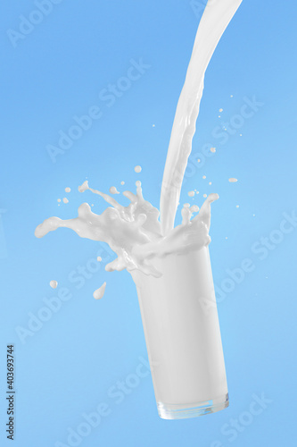 Pouring milk into glass cup with splashing on blue background