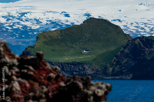 A shot of a lone house on the Elliðaey island in South Iceland near Vestmanaeyjar with Eyjafjallajokull glacier in the background. photo