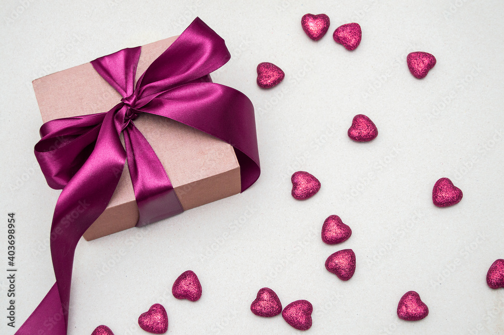 gift in a craft package with a pink bow and pink shiny hearts scattered on a light background, top view. Valentine's Day card with space for text gift in a craft package with a pink bow and pink shiny hearts scattered on a light background, top view. Valentine's Day card with space for text