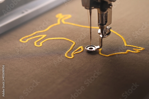 The embroidery of an golden ox symbol on shiny olive green fabric is nearly finished by an modern embroidery machine in bright sunny light - selective focus chinese new year concept