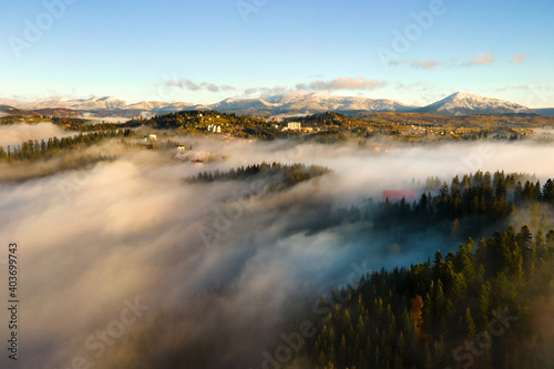 Fototapeta Naklejka Na Ścianę i Meble -  Aerial view of a small distant village houses on hill top in fall foggy mountains at sunrise.