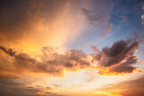 Dramatic sunset landscape with puffy clouds lit by orange setting sun and blue sky.