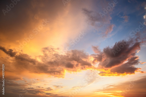 Dramatic sunset landscape with puffy clouds lit by orange setting sun and blue sky. © bilanol