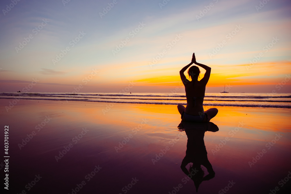 Yoga woman silhouette, practicing on the ocean side of awesome sunset.