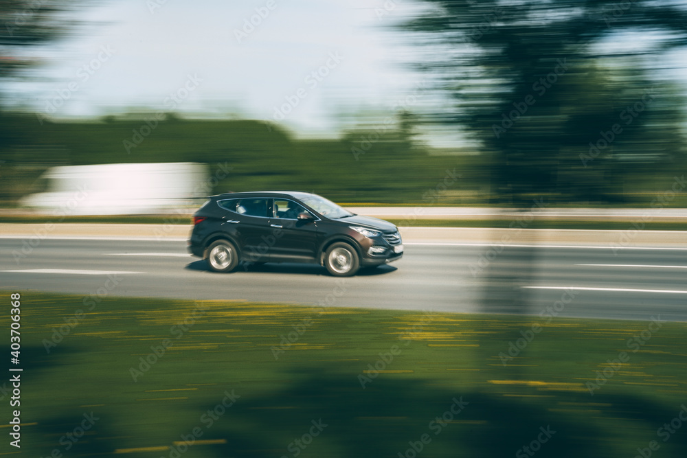 A dark SUV drives along an asphalt road in the summer among the greenery