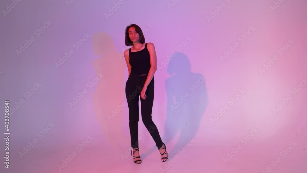 girl in black pants and a black T-shirt on a pink background posing stepping from foot to foot girl in black pants and a black T-shirt on a pink background posing stepping from foot to foot