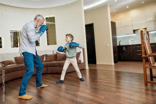 Mature man grandfather wearing boxing gloves practicing punches with little grandson. Physical activity for kids at home © Svitlana