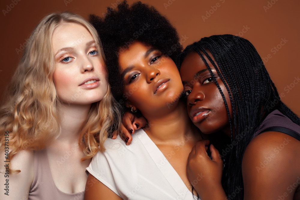 Obraz premium young pretty caucasian, afro, scandinavian woman posing cheerful together on brown background, lifestyle diverse nationality people concept