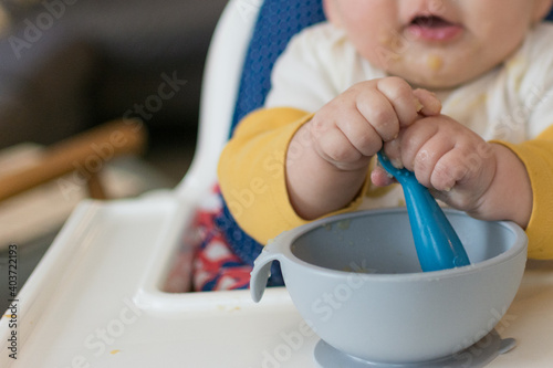 6 month old baby in high chair grasping spoon with two hands while self feeding  photo