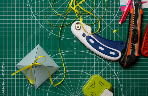 Homemade gift box on a green cutting mat with scrapbooking tools.