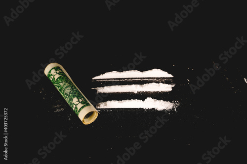 Cocaine powder with rolled dollar banknote on the black table. Narcotics concept. Close-up macro shot. Horizontal shot. High resolution sharp photo.