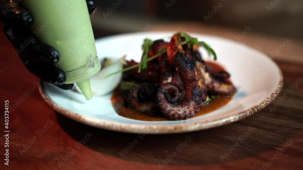 Chef dressing tentacle octopus plate with avocado mousse dressing mexican seafood Chef dressing tentacle octopus plate with avocado mousse dressing mexican seafood