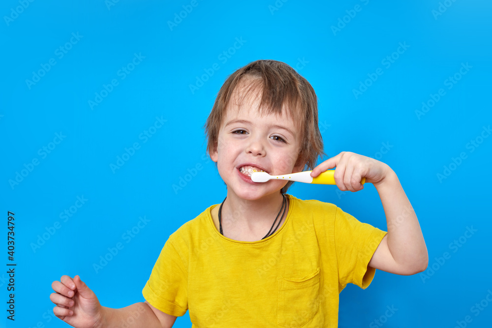 Smiling handsome little boy is brushing his teeth with brush on blue background Smiling handsome little boy is brushing his teeth with brush on blue background