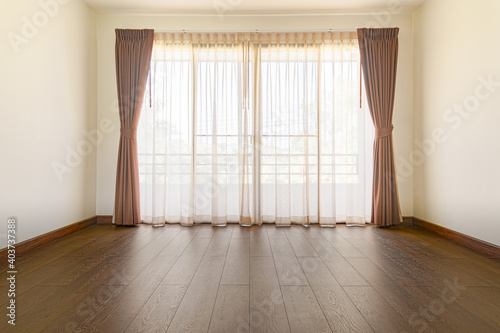 The empty room has wooden floors and curtains.