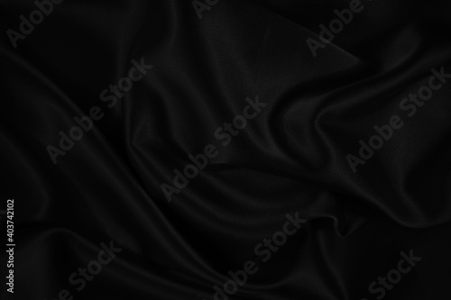 Black silk satin background. Dark elegant abstract background. Wavy soft folds on the fabric.
