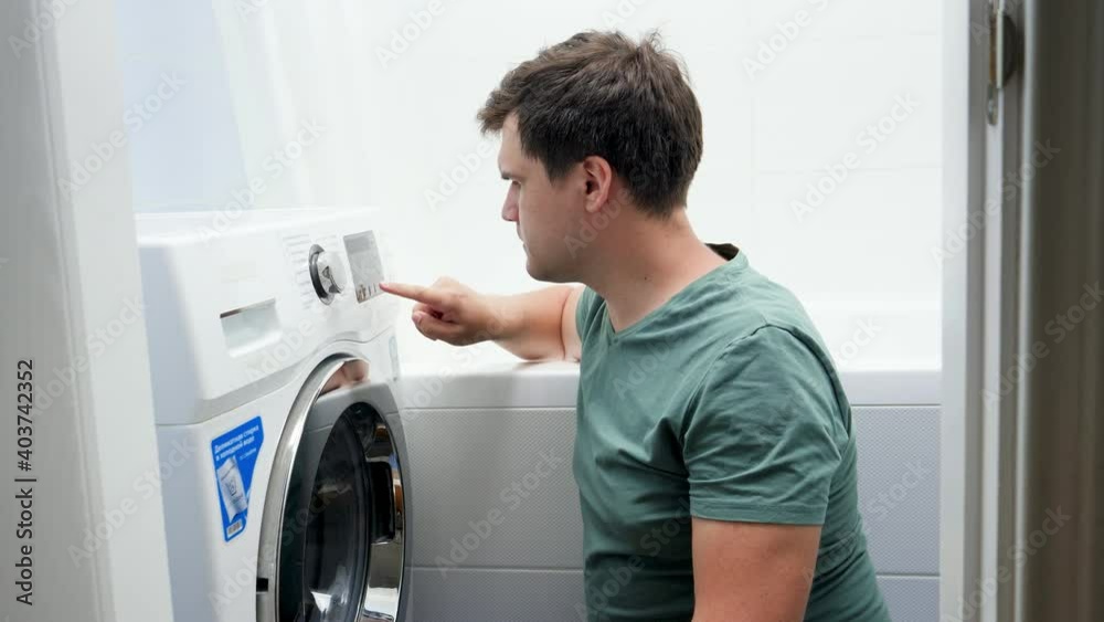 Portrait of young man struggling and getting confused while setting washing machine for laundry Portrait of young man struggling and getting confused while setting washing machine for laundry