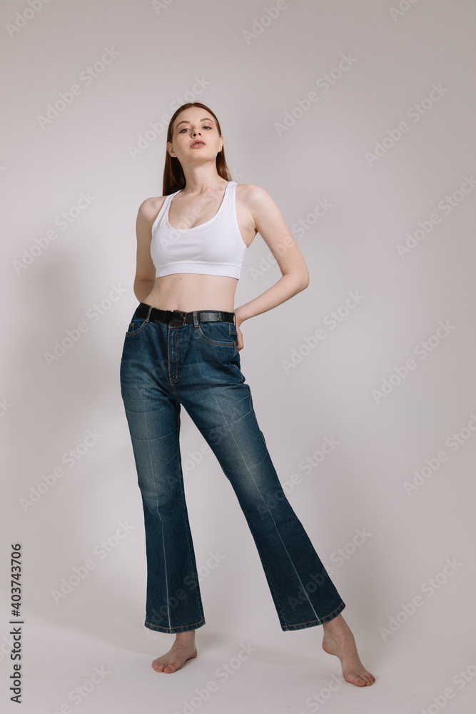 Girl in jeans and barefoot posing on a white background Girl in jeans and barefoot posing on a white background