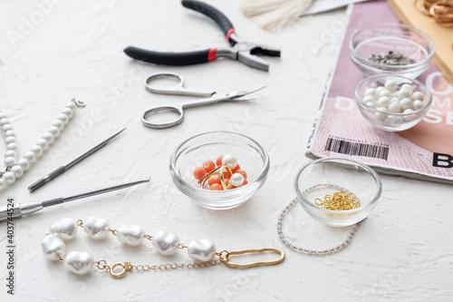 Workplace of jewelry designer with tools and beads on light background