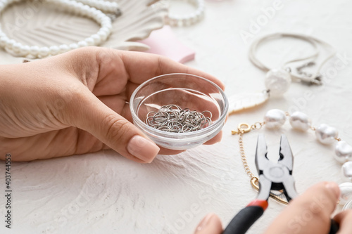 Female designer making jewelry on light background
