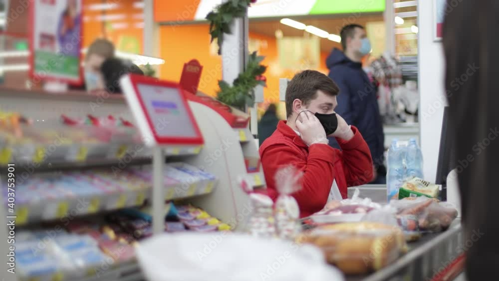 A male salesman, a cashier in a supermarket, examines and corrects his medical mask. Improper use of medical protective masks. A male salesman, a cashier in a supermarket, examines and corrects his medical mask. Improper use of medical protective masks.