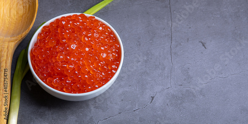 Red caviar in a wooden cup on a grey background with a spoon.