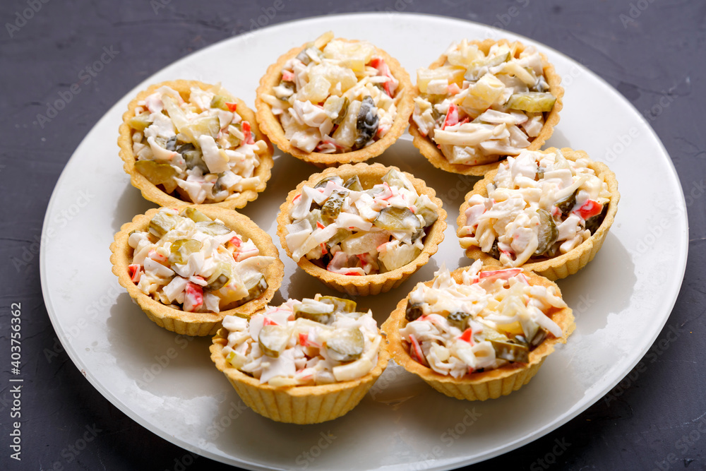 Tartlets with salad on a white plate on a dark background.