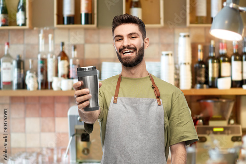 people, profession and job concept - happy smiling waiter in apron holding tumbler or takeaway thermo cup over bar background