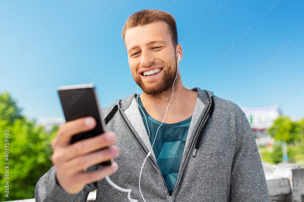 fitness, sport and technology concept - happy smiling young man with earphones and smartphone listening to music outdoors fitness, sport and technology concept - happy smiling young man with earphones and smartphone listening to music outdoors