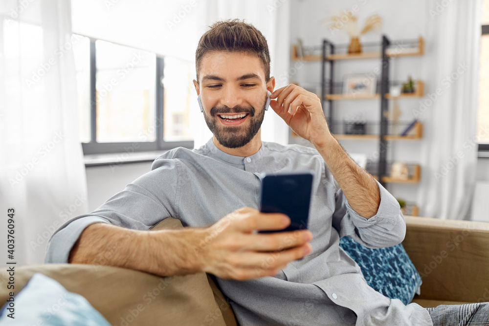 technology, leisure and people concept - happy man in earphones with smartphone listening to music at home technology, leisure and people concept - happy man in earphones with smartphone listening to music at home