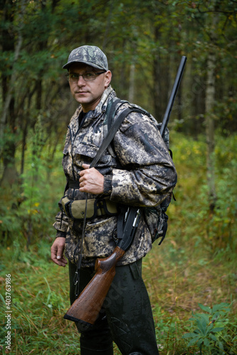 Man hunter standing with shotgun rifle outdoors preparing for bird hunt in autumn forest.