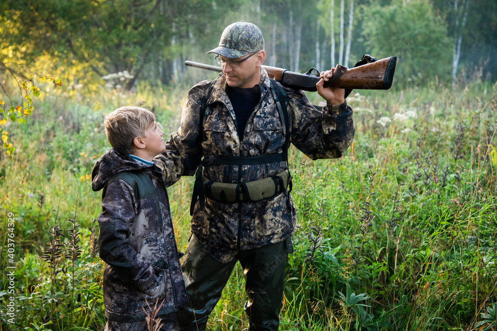 Father and son standing together outdoors with shotgun hunting gear. Father and son standing together outdoors with shotgun hunting gear.