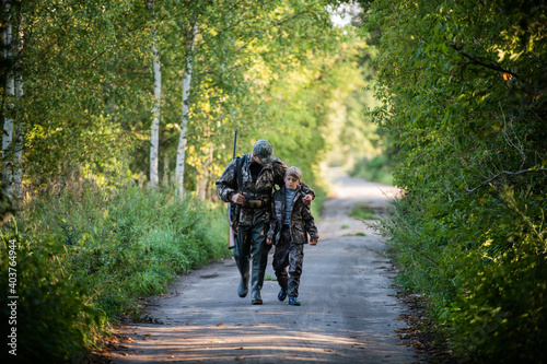 Hunters with hunting equipment going away through rural forest at sunrise during hunting season in countryside.