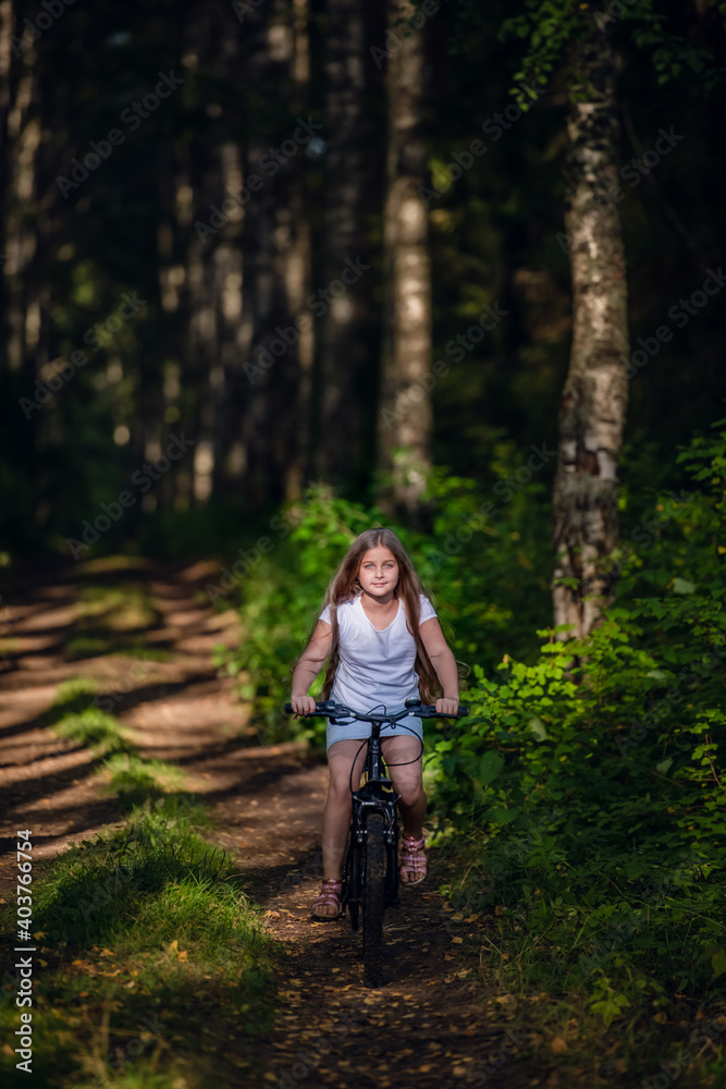 Children girl riding bicycle outdoor in forest smiling.