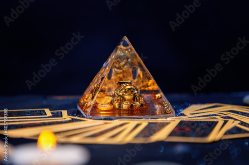 A glass pyramid with a Golden frog. Tarot cards are scattered on the table. Close-up. Copy space. The concept of divination, magic and esotericism