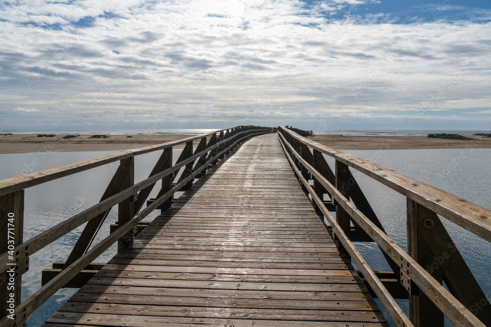 long wooden boardwalk pier leads from one beach to another over a small ocean inlet