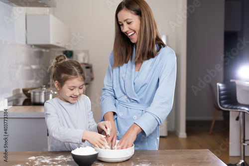 mom and daughter together in the kitchen knead dough in a bowl. Cooking concept together at home.