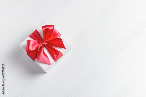 White present box tied with red beautiful bow on white background. Top view, copy space.