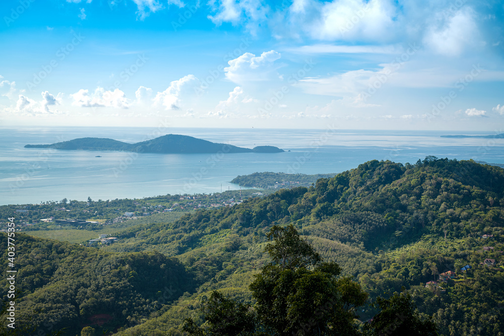 The landscape of the mountain ridge of Phuket and the Adaman Sea against the background of a blue sky with clouds.
