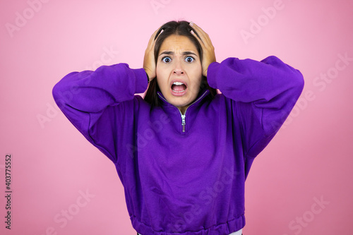 Young beautiful woman wearing sweatshirt over isolated pink background crazy and scared with hands on head, afraid and surprised of shock © Irene