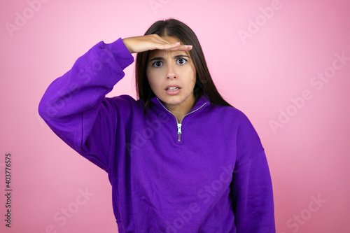 Young beautiful woman wearing sweatshirt over isolated pink background very happy and smiling looking far away with hand over head. searching concept. © Irene