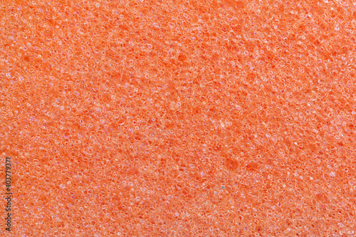 Orange foam kitchen sponge texture. Full frame macro photography of porous synthetic material. Abstract pattern background for cleaning and housework. Close-up design element.
