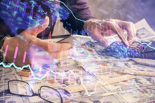 Double exposure of man's hands holding and using a digital device and forex graph drawing. Financial market concept.