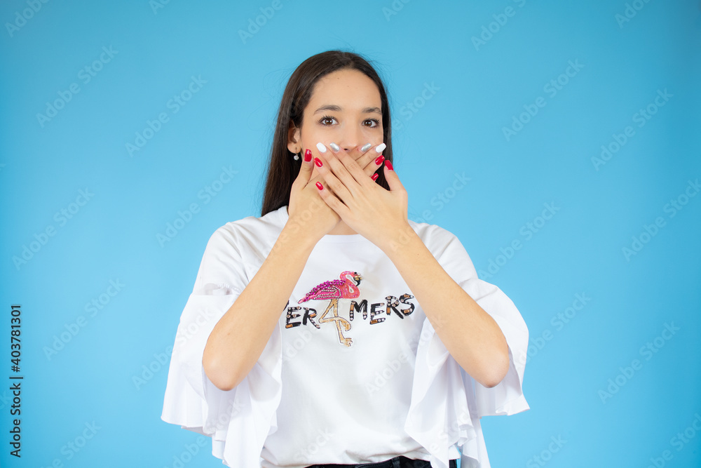 Portrait of a surprised young woman covering mouth with hands isolated over blue background Portrait of a surprised young woman covering mouth with hands isolated over blue background